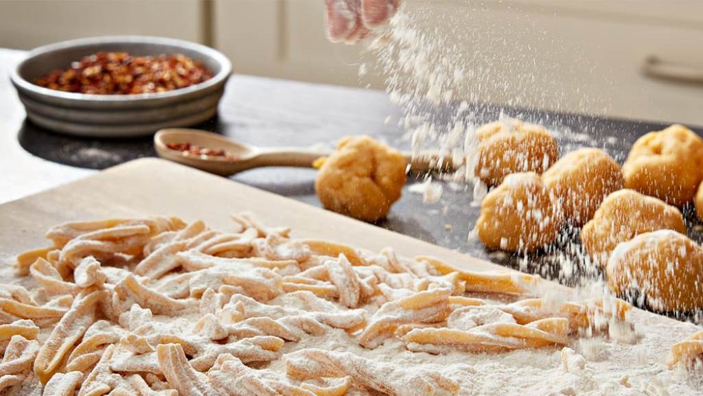 Fresh homemade fettuccine nests dusted with flour next to KitchenAid pasta cutter set