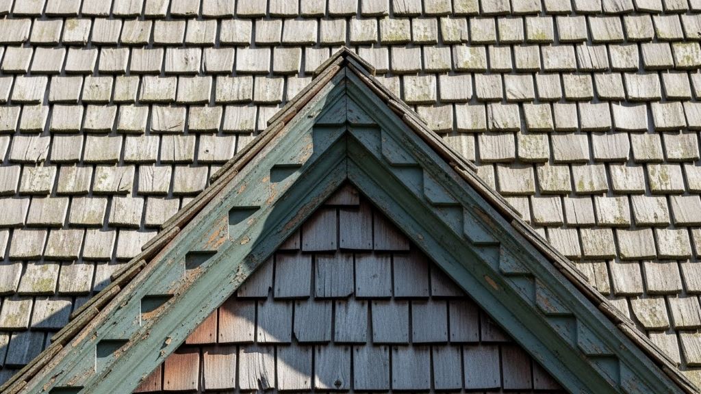 Close-up detail of colonial-era wooden shingle gable roof showing weathered cedar shakes and decorative trim